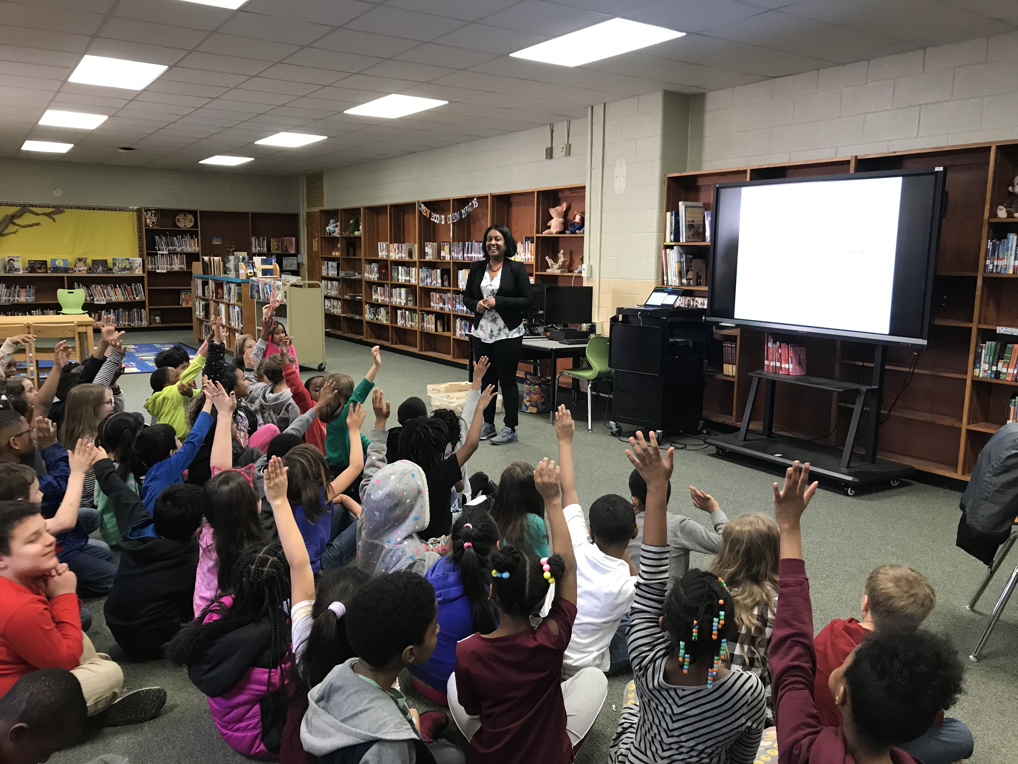 Students raising hands during a library lesson on algorithms